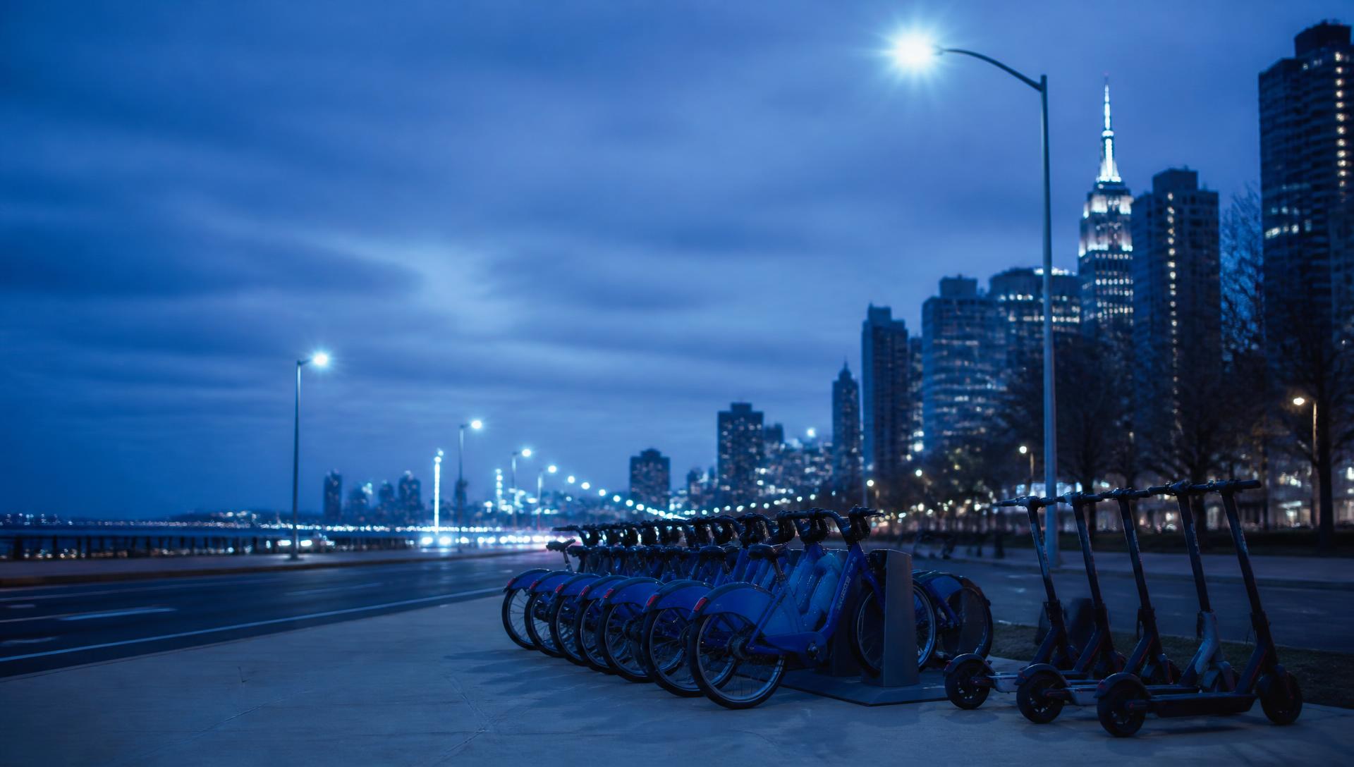 Shared bikes and electric scooters parked along a New York City street at sunset